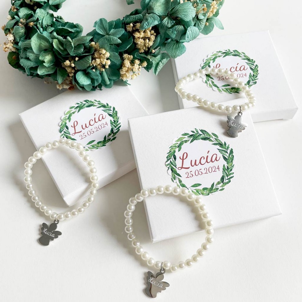 Tres pulseras de perlas blancas con dije de ángel grabado junto a cajas con etiquetas de corona de hojas